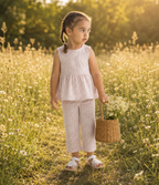 Young girl in a checkered outfit standing in a field with a basket of flowers.